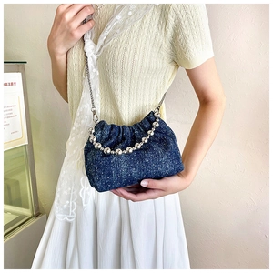 Close-up of blue denim cloud bag with metal bead handle and pleated texture detail