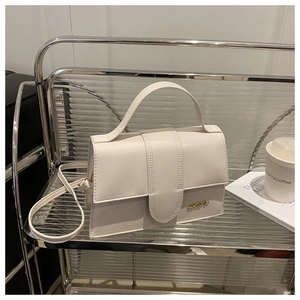 Détail du sac à rabat en cuir blanc avec logo doré et coutures sur un chariot en verre
