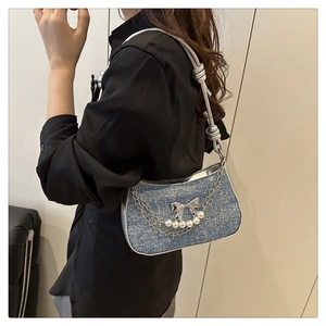 Détail du sac à bandoulière en denim bleu avec chaîne de perles et papillon argenté