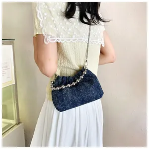 Detail of blue denim bucket bag featuring silver bead handle and metal chain strap