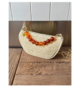 Detail of cream straw half-moon bag with amber bead chain and metallic shoulder strap