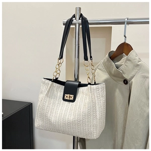 Detail of woven straw tote bag featuring black leather flap and gold twist lock closure