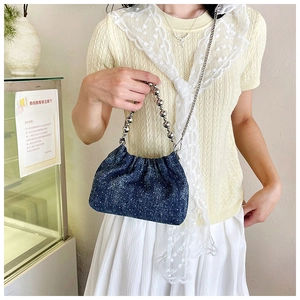 Close-up of a blue denim drawstring bucket bag with silver metal bead handle and chains