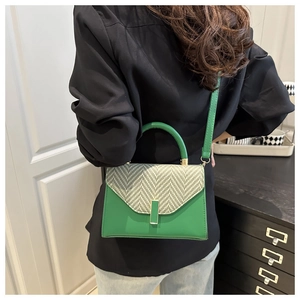 Detail showing green leather crossbody bag with herringbone weave and gold buckle on a model