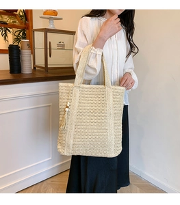 Detailed close-up of a beige woven straw tote bag with decorative tassels and wood beads
