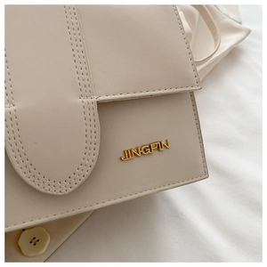 Gros plan du sac à rabat crème avec logo JINGPIN doré et détails de couture élégants