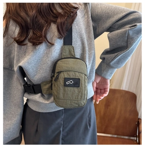 Dettaglio del borsello monospalla in nylon verde militare indossato su una felpa grigia