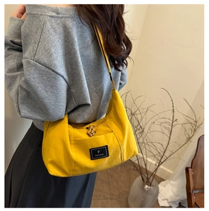 Detail of bright yellow canvas shoulder bag featuring a black brand logo and unique rope knot zipper