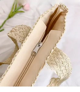 Detail of the sturdy metal zipper pull and woven texture on a beige straw tote bag