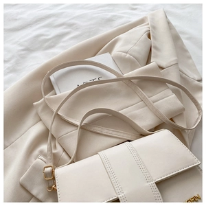 Détail du sac crème avec coutures parallèles et plaque logo en métal doré élégant