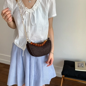 Brown woven crossbody bag with amber beads and gold chain on a stylish model