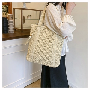 Detail of hand-woven straw tote bag with fringe tassels on model in a modern cafe