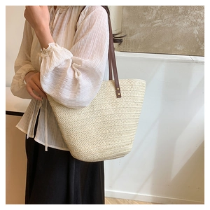 Detail shot of hand-woven straw tote bag texture with brown leather strap and metal rivets