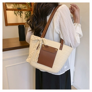 Grand sac cabas en paille crème avec poche cuir et nœud en dentelle porté par un mannequin