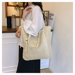 Detail of hand-woven straw tote bag featuring decorative fringe and wooden bead pendant