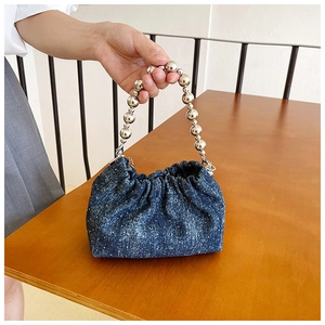 Detail of blue denim bucket bag featuring silver ball chain handle and pleated drawstring