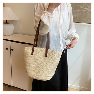 Detail of hand-woven straw tote bag with brown leather straps and metal rivets