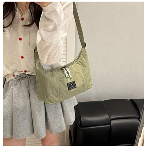 Green pleated nylon tote bag shown on a model in a minimalist indoor setting