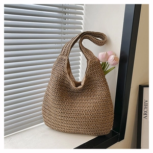 Detail of woven straw shoulder bag with natural texture and integrated wide strap on window sill