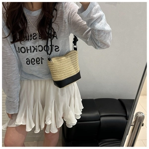 Détail du sac seau en paille tressée avec base en cuir noir et bandoulière fine
