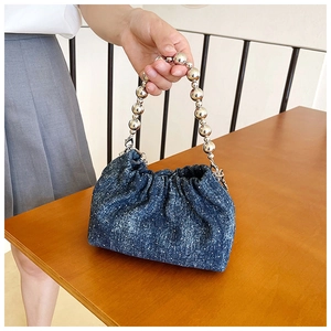 Detailed view of blue denim pleated handbag with silver beaded handle on wooden table