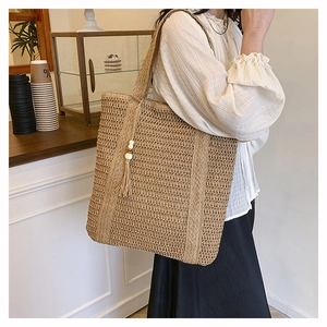 Detail of hand-woven straw tote bag with decorative tassel and wooden bead charm