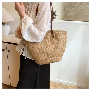 Detail of woven straw tote bag with brown leather straps and metal rivets on model