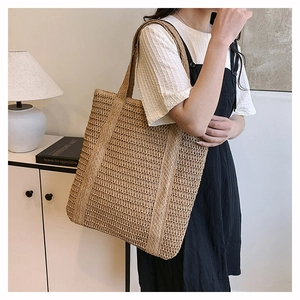 Detail of hand-woven straw tote bag showing hollow mesh texture and wide strap