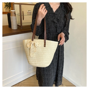 Detail of beige woven straw tote with leather handles and lace bow on a floral dress