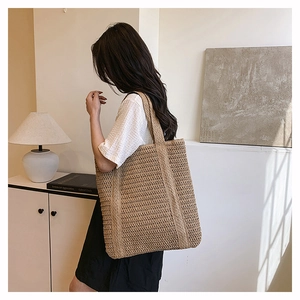 Detail of hand-woven straw tote bag showing intricate hollow pattern and wide shoulder strap