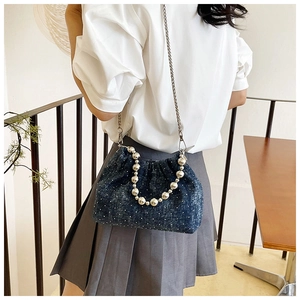 Detail of dark blue denim bucket bag with pearl handle and white polka dots on shoulder