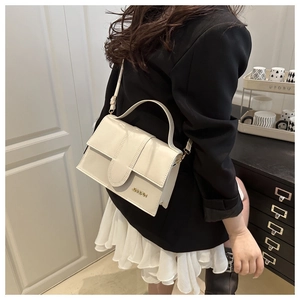 Détail d'un sac à main beige en cuir avec logo doré porté à l'épaule, vue de profil élégante