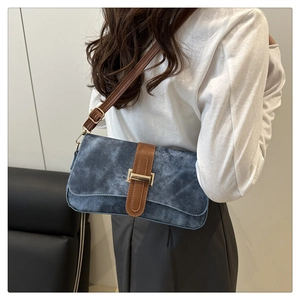 Détail du sac baguette en denim bleu avec bandoulière en cuir brun et boucle dorée