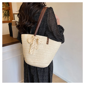 Detail view of woven straw tote bag with brown straps and a decorative lace bow