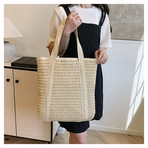 Close-up of a large beige hand-woven tote bag showing intricate straw texture and shoulder strap