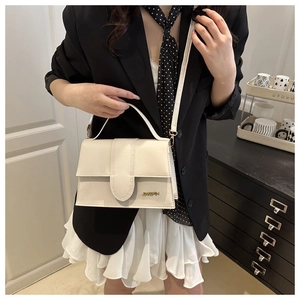 Sac à rabat chic blanc cassé avec logo métallique porté en bandoulière en intérieur