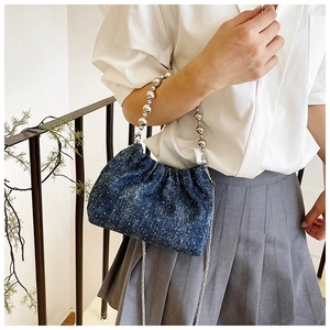 Detail of blue denim bucket bag with white dots and silver bead handle on metal chain