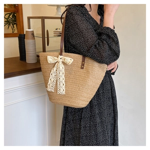 Detail of handwoven straw tote with large white lace bow and brown leather strap