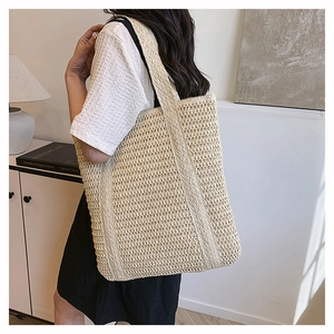 Close-up of cream woven straw tote bag with wide shoulder straps in a modern room setting
