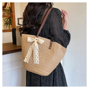 Detail of woven straw tote bag with large white lace bow and brown leather shoulder straps