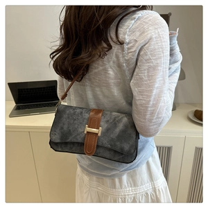 Détail du sac baguette gris vintage avec bandoulière en cuir marron et boucle dorée élégante