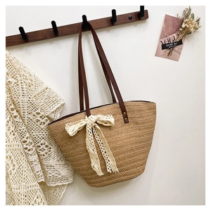 Detail of straw tote bag featuring a white lace bow and brown leather handle