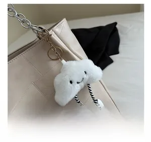 Detail of white plush cloud keychain with smile embroidery on a woven handbag