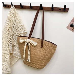 Detail of woven straw tote bag featuring brown leather handles and a lace bow accent