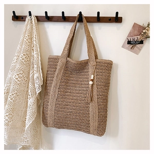 Detail of handmade woven straw tote bag with wood bead tassel on a wooden hanger