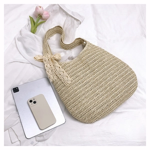 Flat lay of beige woven beach tote bag with a lace bow on soft white fabric