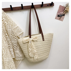 Detail of woven straw tote bag featuring a cream lace bow and brown leather shoulder straps