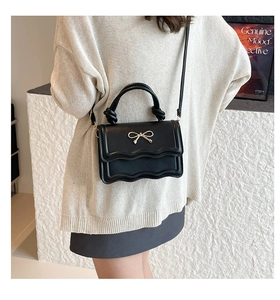 Detail der schwarzen Ledertasche mit gewellter Klappe, Schleife und geknotetem Griff