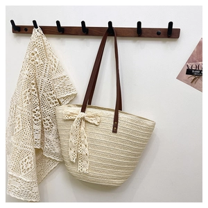 Close-up of woven tote bag featuring a delicate lace bow and brown leather shoulder strap