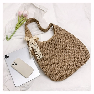 Close-up of woven straw tote bag with white lace bow detail on a clean white surface